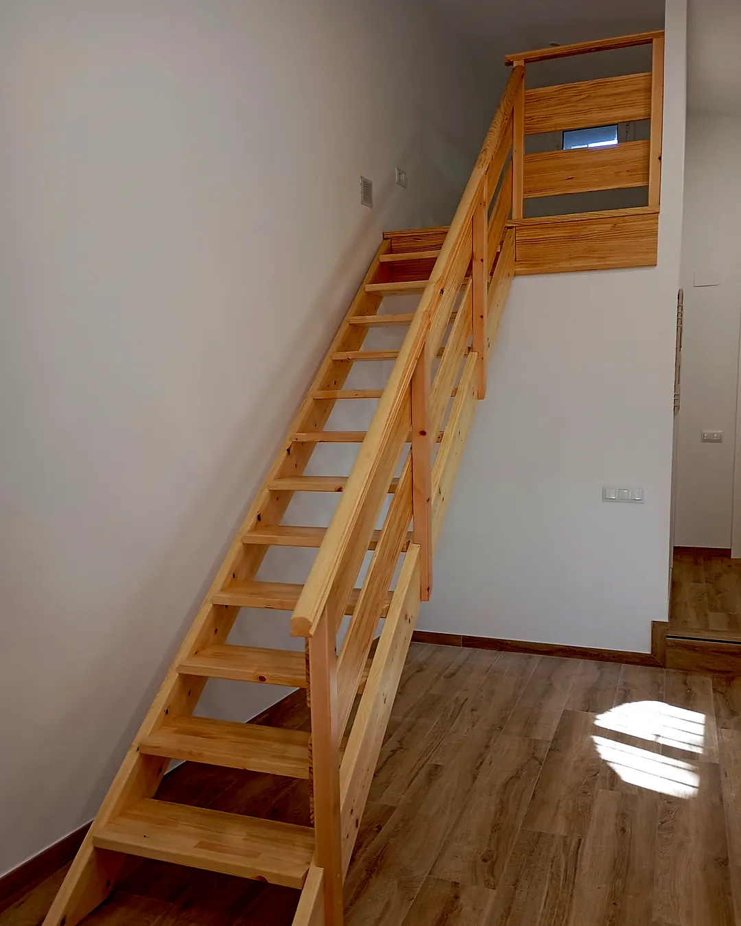 Escala de fusta de pi massís amb barana i passamà fins a un altell