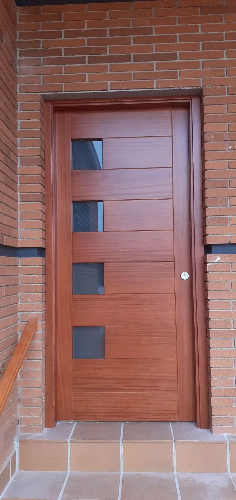Porta de fusta amb vidres a una façana de maó vist